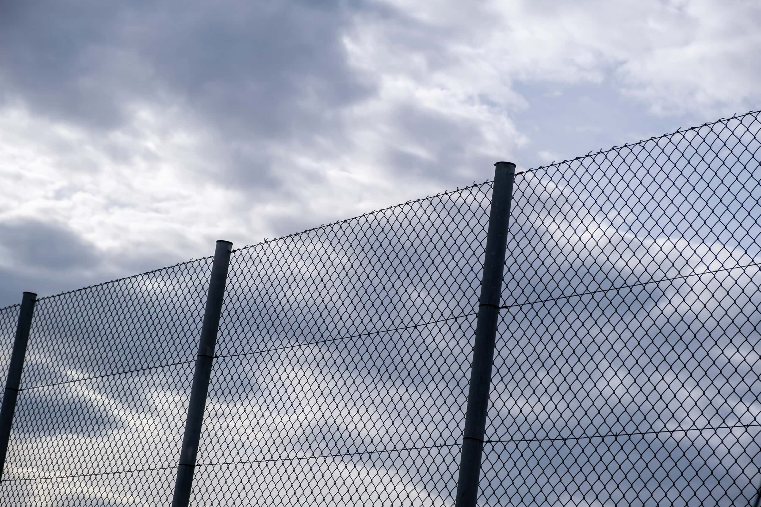 Wire mesh fence on cloudy sky background, low angle view. Metallic barrier, safety and security concept